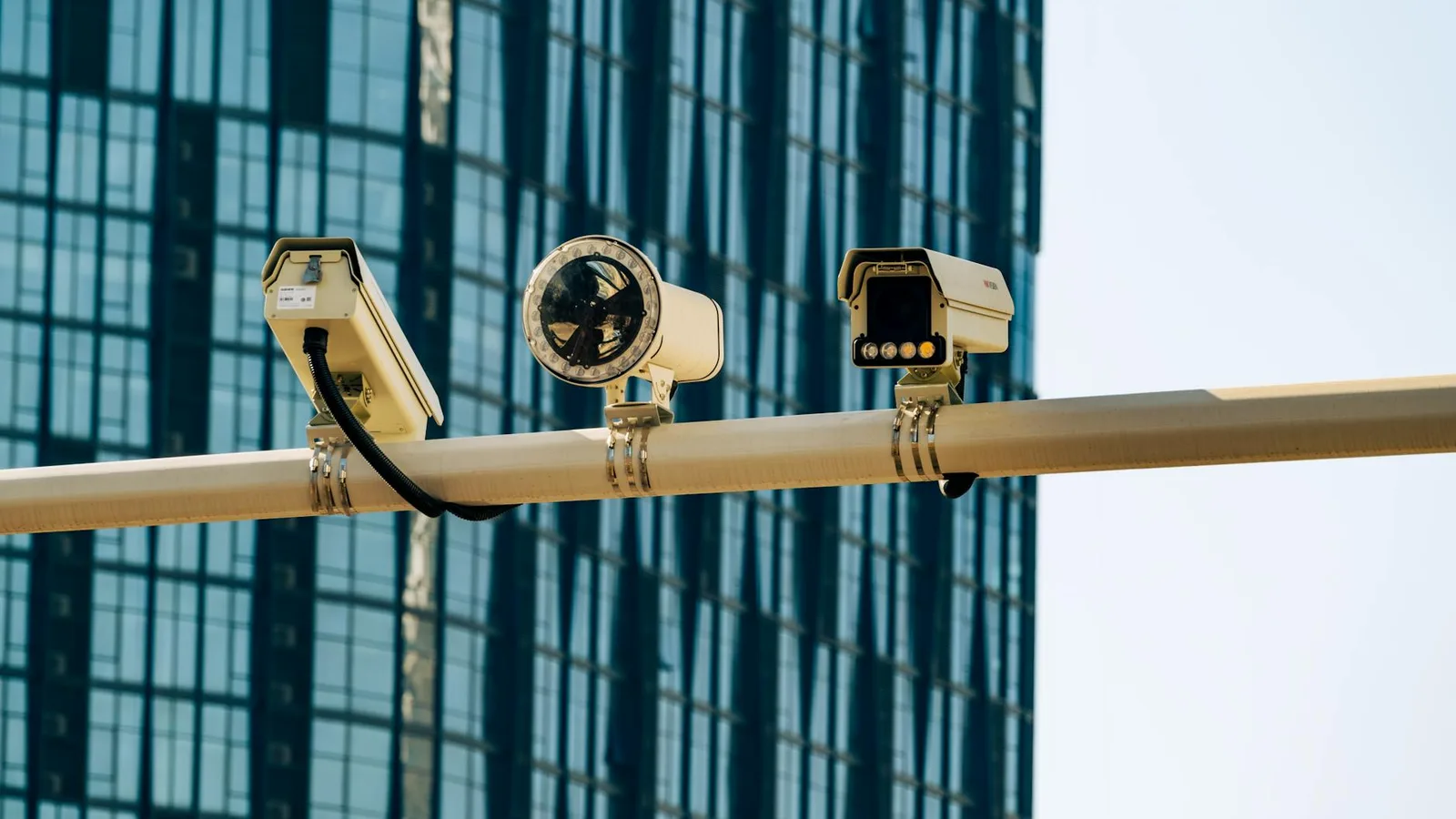 Surveillance cameras mounted on a pole in front of a modern glass building.