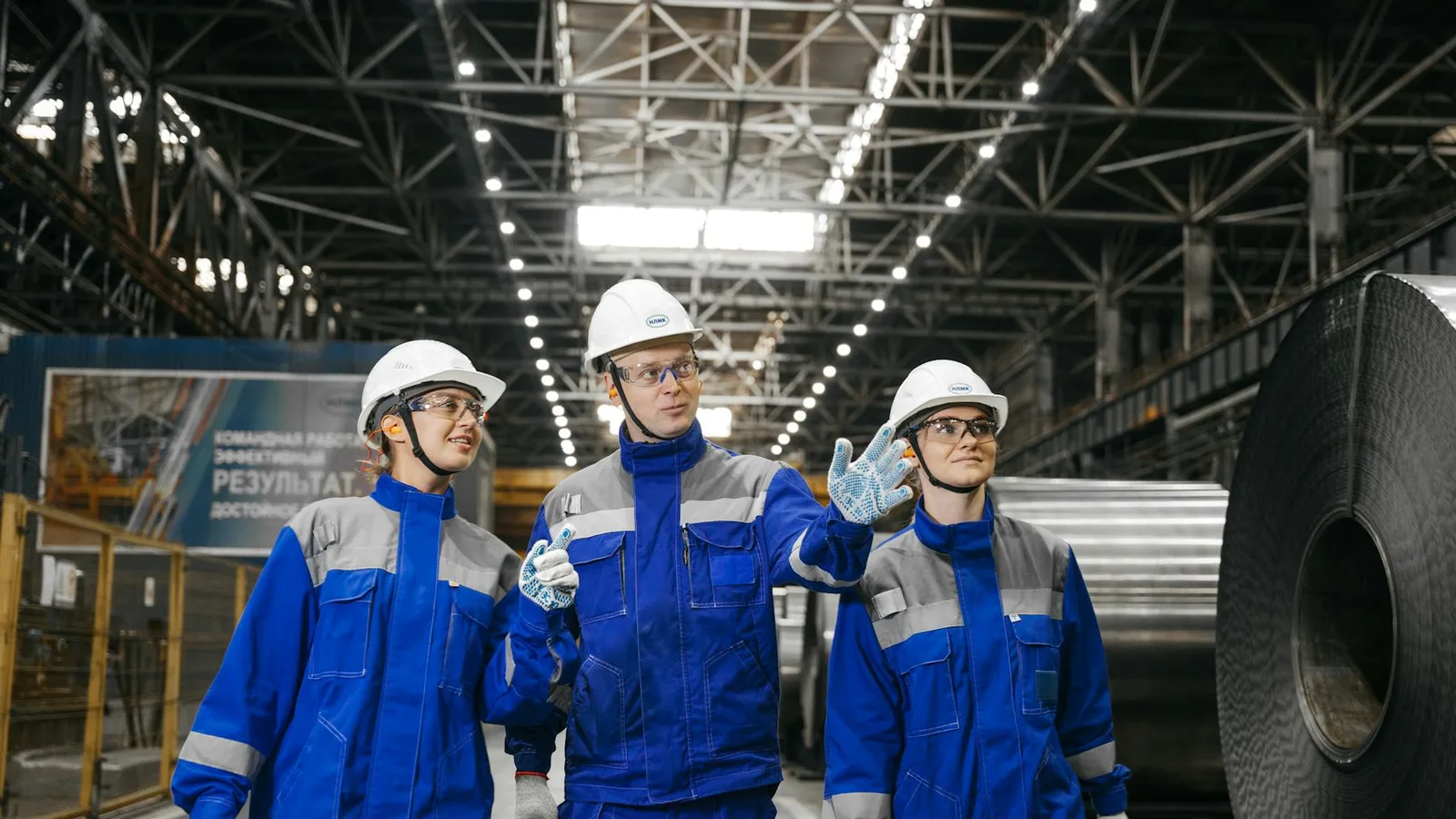 Group of workers in safety gear inside an industrial steel factory, engaging in discussion.