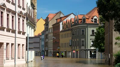 Street flooding in a European city with historic architecture under a sunny sky.