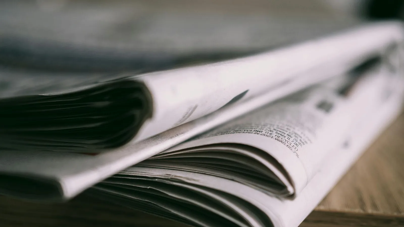 Stack of folded newspapers on a wooden table with a focus on printed pages.